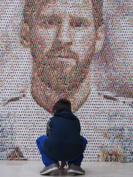 Seorang bocah memperhatikan mural Lionel Messi di Casa Rosada Museum, Buenos Aires, Argentina, Rabu (20/6). Mural terbuat dari dua ribu stiker figur pemain Argentina dalam Piala Dunia sepanjang masa. (Eitan ABRAMOVICH/AFP)