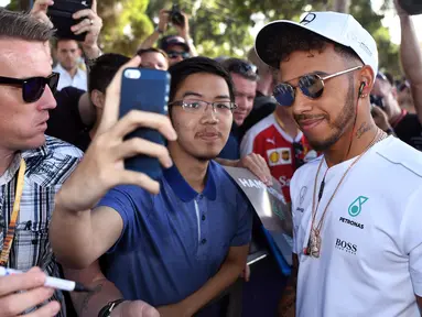 Pembalap Mercedes, Lewis Hamilton melakukan selfie dengan seorang penggemar menjelang sesi latihan bebas pertama di Grand Prix Australia, Melbourne, Jumat (24/3). (AFP Photo/WILLIAM WEST)