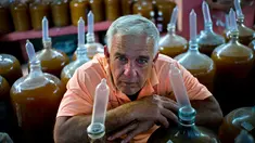 Pembuat minuman wine, Orestes Estevez berpose di dekat kendi berisikan anggur buatannya di Havana, Kuba, Kamis (30/3). Orestes menggunakan kondom sebagai penutup kendi dari anggur racikannya. (AP Photo)