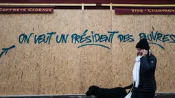 Seorang wanita berjalan melewati grafiti bertuliskan 'kami ingin seorang presiden untuk orang miskin' di sebuah toko dekat Arc de Triomphe, Paris, Prancis,  Minggu (2/12). Tiga orang tewas dalam unjuk rasa sejak dua pekan lalu. (AP Photo/Kamil Zihnioglu)