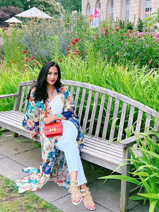 Berpose duduk di bangku taman, Diah Permatasari hadirkan nuansa summer dengan pilihan outfit yang colorful. Atasan dan celana putih, dipadunya lagi dengan long outer bermotif floral bernuansa biru-kehijauan. Ia menambahkan sentuhan sling bag merah sebagai pemanis yang pas untuk penampilannya. Foto: Instagram.