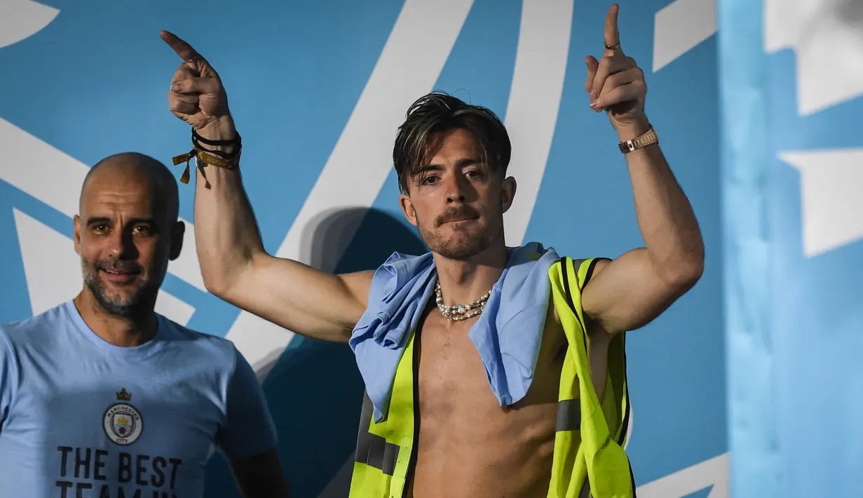 Pemain Manchester City, Jack Grealish (kanan), memasuki panggung dengan mengenakan rompi proyek setelah melakukan parade Treble Winners, Selasa (13/6/2023) dini hari WIB. Pep Guardiola hanya bisa tersenyum melihat kelakuan anak asuhnya tersebut. (AFP/Oli Scarff)
