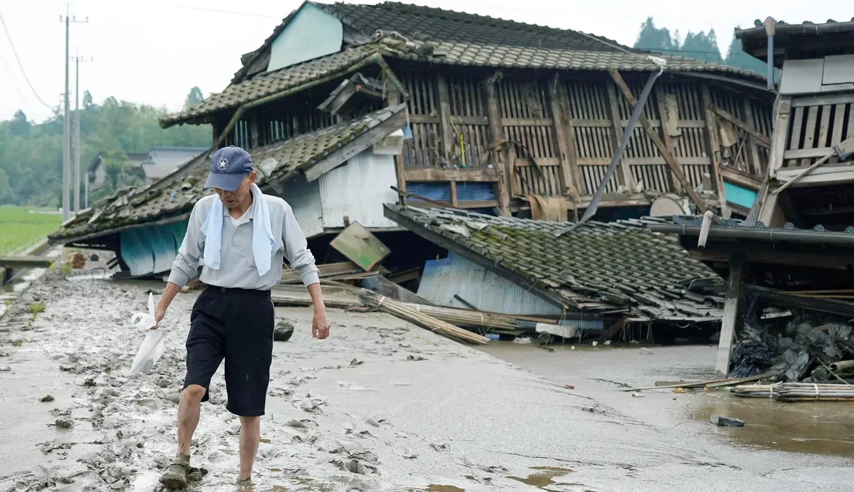 Seorang pria melewati jalan berlumpur dan rumah-rumah yang rusak oleh banjir di Kuma village, prefektur Kumamoto, Jepang, Minggu (5/7/2020). Banjir di wilayah Kumamoto yang memicu tanah longsor ini telah menghancurkan ratusan rumah dan kendaraan serta membuat jembatan terputus. (STR/JIJI PRESS/AFP)