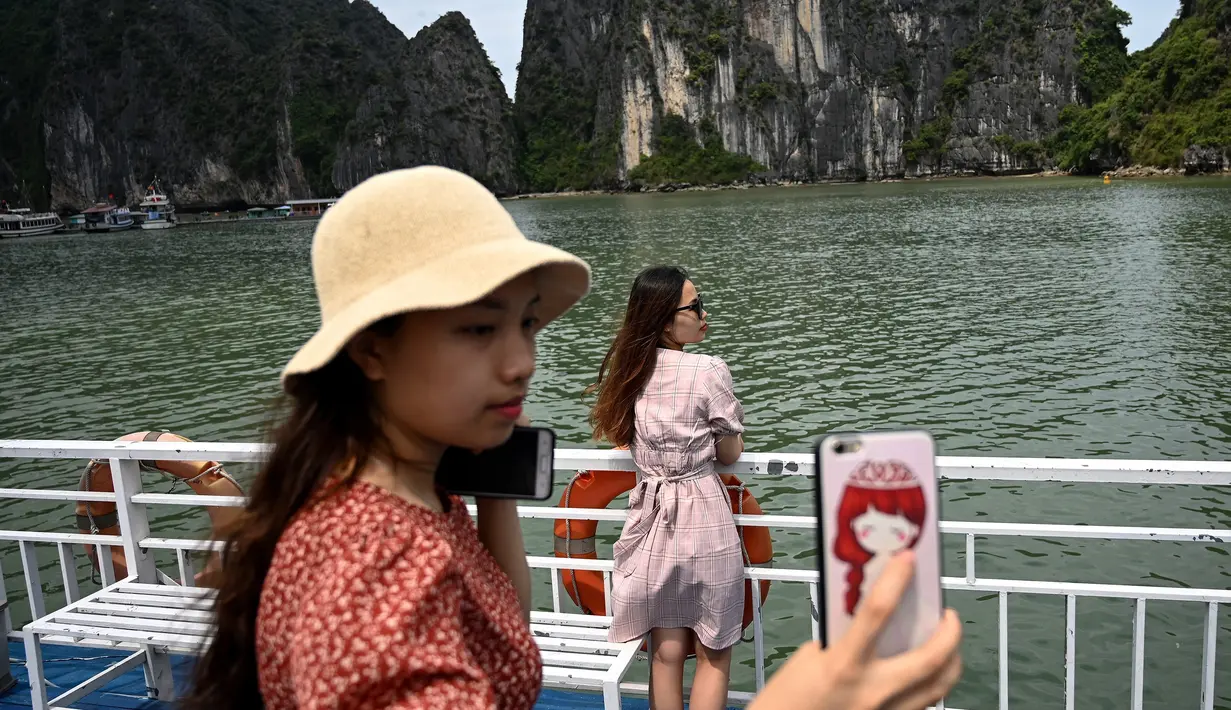 Wisatawan domestik berpose untuk foto di atas kapal di tengah Ha Long Bay, Quang Ninh, Vietnam, (16/5/2020). Sempat terpukul akibat pandemi virus corona Covid-19, pariwisata Vietnam kembali menggeliat setelah otoritas setempat melonggarkan pembatasan perjalanan. (AFP/Manan Vatsyayana)