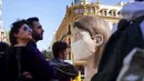 Orang-orang melintasi patung raksasa mengenakan masker yang akan ditampilkan di festival Las Fallas atau festival api di Valencia, Spanyol, Rabu (11/3/2020). Festival Fallas yang akan berlangsung pada 13 Maret telah dibatalkan karena wabah coronavirus. (AP/Alberto Saiz)