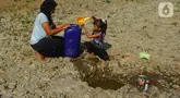 Seorang anak bersama ibunya mengambil air pada galian sumur di tengah aliran Sungai Cihoe, Kamis (28/9/2023). Warga Desa Sukagalih, Jonggol, Bogor, mengalami kesulitan air bersih di tengah fenomena El Nino yang menyebabkan musim kemarau berkepanjangan. (merdeka.com/Arie Basuki)