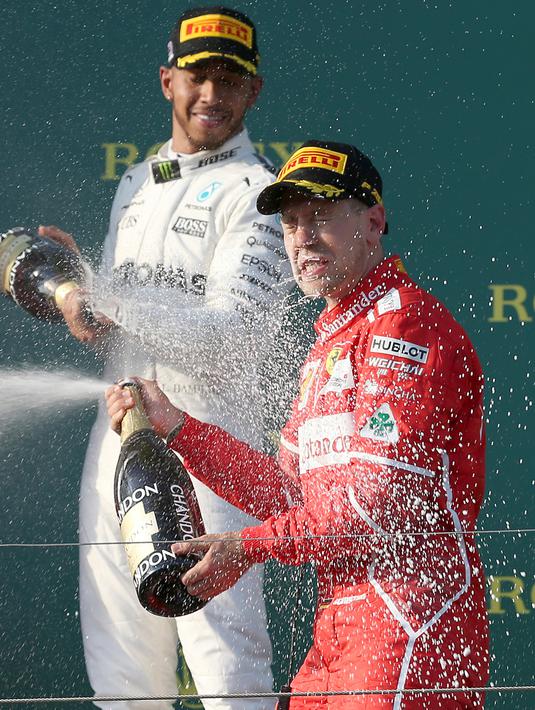 Pembalap Mercedes, Lewis Hamilton menyemprotkan sampanye ke pembalap Ferrari, Sebastian Vettel di atas podium balapan GP Australia di Sirkuit Albert Park, Melbourne, Minggu (26/3). Sebastian Vettel berhasil memenangi GP Australia. (AP Photo/Rick Rycroft)