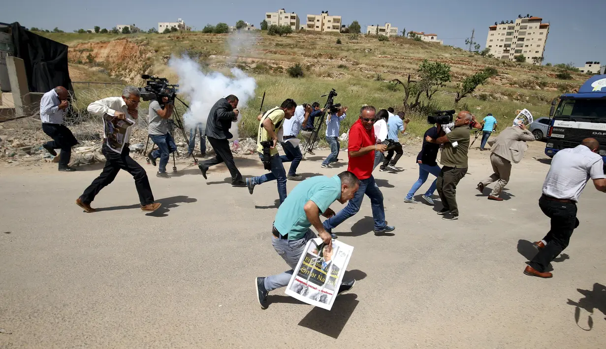 Wartawan Palestina berlari berhamburan setelah gas air mata ditembakkan pasukan Israel saat meliput aksi protes yang menyerukan pembebasan wartawan Palestina, Omar Nazzal di dekat Penjara Ofer Israel di Ramallah, Israel (26/4).(REUTERS / Mohamad Torokman)