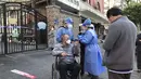 Pekerja dengan alat pelindung membantu seorang pria di kursi roda selama pengujian massal untuk penduduk di distrik Jingan, Shanghai barat (4/4/2022). China telah mengirim lebih dari 10.000 petugas kesehatan dari seluruh negeri ke Shanghai, termasuk 2.000 staf medis militer. (AP Photo/Chen Si)