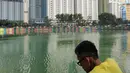 Seorang warga mengamati Danau Sunter yang berwarna hijau di Jakarta Utara pada Senin (8/7/2019). Lamanya musim kemarau di Ibu kota menjadi penyebab danau tersebut berubah warna menjadi hijau yang dipicu oleh pertumbuhan lumut. (Liputan6.com/Immanuel Antonius)