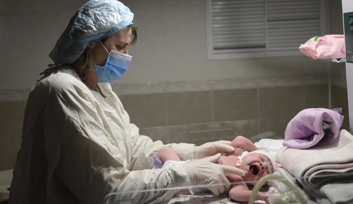 Seorang perawat memeriksa bayi Aleina Snizhana yang melahirkan di bangsal bersalin saat peringatan sirene untuk serangan udara di Mykolaiv, Ukraina pada 14 Maret 2022. Hampir setengah dari 49 perempuan harus melahirkan di ruang bawah tanah sejak 24 Februari lalu. (BULENT KILIC/AFP)