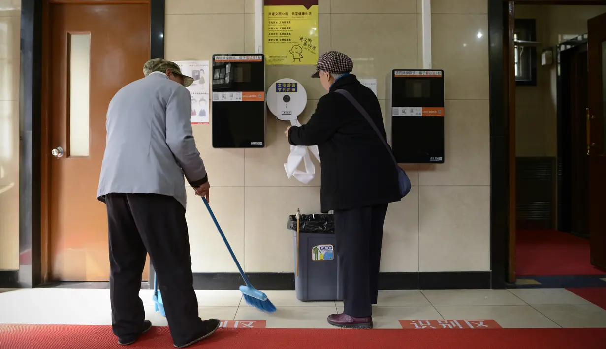 Pengunjung mengambil tisu yang dipasangi alat pendeteksi wajah di toilet umum di Temple of Heaven, Beijing, China, Selasa (21/3). Alat ini dipasang setelah banyak warga lansia Beijing yang mencuri tisu toilet untuk digunakan di rumah. (WANG Zhao/AFP)