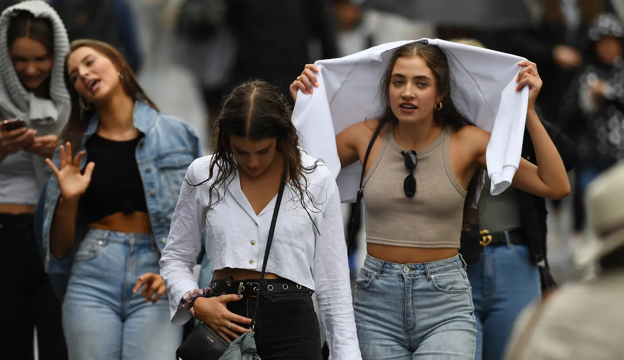 Penonton berjalan di tengah hujan pada hari pertama turnamen tenis Australia Terbuka di Melbourne, Senin (20/1/2020). Pertandingan Roger Federer melawan Steve Johnson sempat terhenti akibat hujan deras yang mengguyur Rod Laver Arena.  (AFP Photo/Greg Wood)