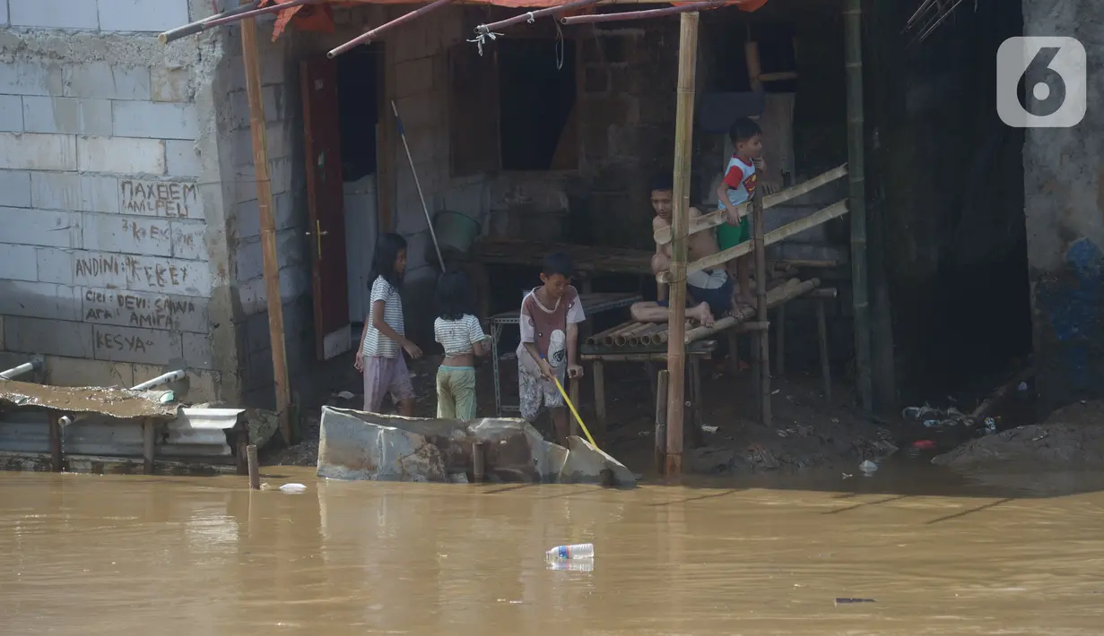Anak-anak membersihkan rumah dari sisa lumpur di Bukit Duri, Jakarta, Jumat (29/10/2021). Hujan dengan intensitas tinggi beberapa hari lalu membuat aliran sungai ciliwung meluap yang merendam sebagian rumah warga yang tinggal di bantaransungai  tersebut. (merdeka.com/Imam Buhori)