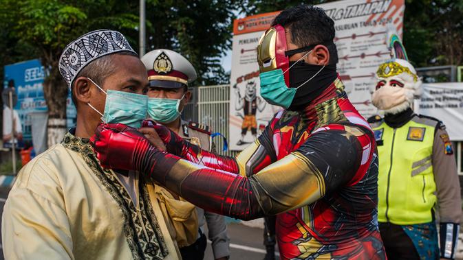 Petugas kepolisian berpakaian superhero memakaikan masker kepada warga di jalan kawasan Pasuruan, Jawa Timur, Kamis (9/4/2020). Hal tersebut bertujuan untuk mengantisipasi penyebaran Virus Corona (COVID-19). (JUNI KRISWANTO / AFP)