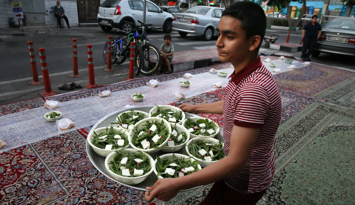 Seorang relawan menyiapkan makanan berbuka di sebuah jalan di Teheran, 29 Mei 2018. Sebagian besar warga muslim Iran melaksanakan ibadah puasa di bulan Ramadan sesuai ajaran Islam melalui Nabi Muhammad. (AP Photo/Vahid Salemi)