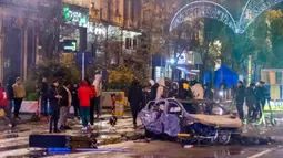 Orang-orang berdiri di samping mobil yang terbakar saat kerusuhan di Brussel, Belgia, 27 November 2022. Polisi harus menutup sebagian pusat Kota Brussel dan bergerak dengan meriam air serta gas air mata untuk membubarkan massa menyusul kerusuhan selama dan setelah Maroko menang 2-0 atas Belgia di Piala Dunia 2022. (AP Photo/Geert Vanden Wijngaert)