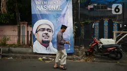 Warga berjalan di depan poster Rizieq Shihab di Jalan Petamburan 3, Jakarta, Rabu (30/12/2020). Pemerintah memutuskan untuk menghentikan kegiatan dan membubarkan organisasi massa Front Pembela Islam (FPI). (merdeka.com/Imam Buhori)