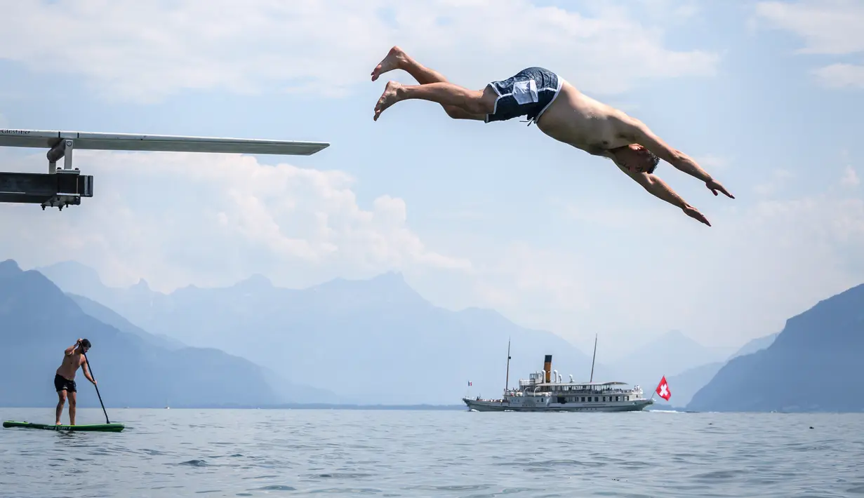 Seorang pria melompat ke Danau Jenewa di Saint Saphorin, Swiss barat saat gelombang panas melanda seluruh Eropa utara (31/7). Akibat gelombang panas suhu di beberapa bagian Swiss mencapai 35 Derajat. (AFP Photo/Fabrice Coffrini)