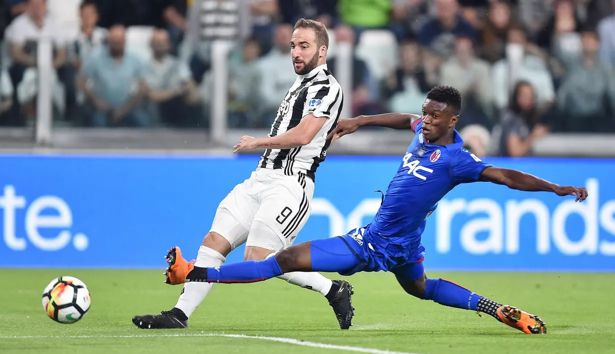 Pemain Juventus, Gonzalo Higuain (kiri) melepaskan tembakan melewati adangan pemain Bologna, Ibrahima Mbaye pada lanjutan Serie A di Allianz Stadium, Turin, (5/5/2018). Juventus menang 3-1. (Alessandro Di Marco/ANSA via AP)