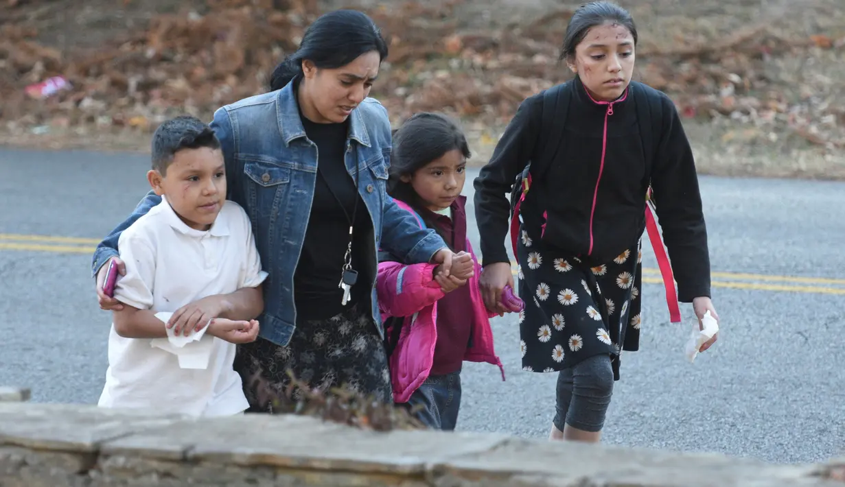 Seorang wanita membawa tiga orang anak menjauh dari lokasi kecelakaan bus sekolah di Chattanooga, Tennessee, Senin (21/11). Belum ada kejelasan penyebab kecelakaan bus yang ditemukan terbaring di antara pepohonan itu (Courtesy of Angela Lewis/Chattanooga)