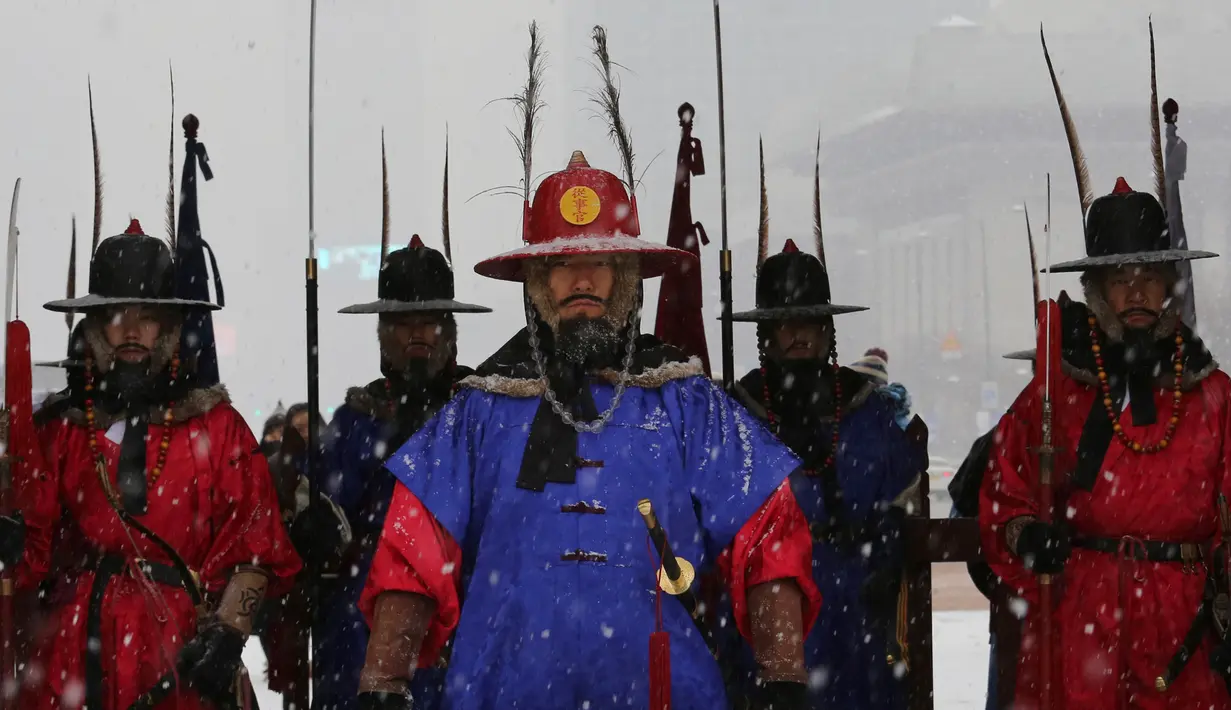 Penjaga istana mengenakan seragam militer tradisional berdiri selama hujan salju di Istana Gyeongbok di Seoul, Korea Selatan (13/12). Istana Gyeongbok aslinya didirikan tahun 1394 oleh Jeong do jeon, seorang arsitek.  (AP Photo/Ahn Young-joon)