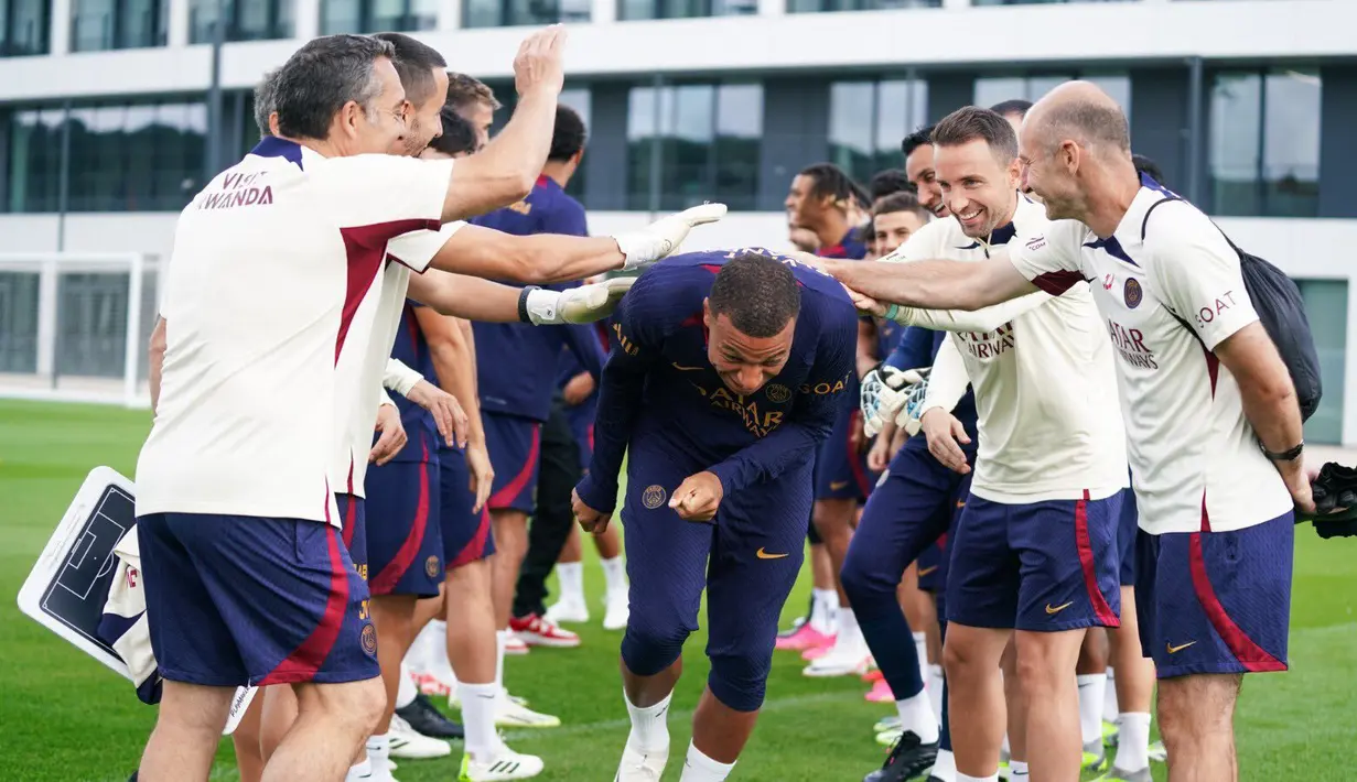 Staf kepelatihan menyambut kedatangan pemain PSG, Kylian Mbappe (tengah), dengan sukacita sebelum menjalani sesi latihan bersama pemain PSG lainnya di Poissy, Senin (14/8/2023). (Twitter/@PSG_English)