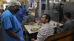 Pelanggan berbincang dengan pramusaji di sebuah restoran yang dibuka kembali usai pelonggaran lockdown di Bangalore, India, Senin (8/6/2020). Untuk keamanan pelanggan, restoran-restoran menyiapkan panel transparan di meja makan sebagai bagian dari rangkaian pencegahan COVID-19. (Manjunath Kiran/AFP)