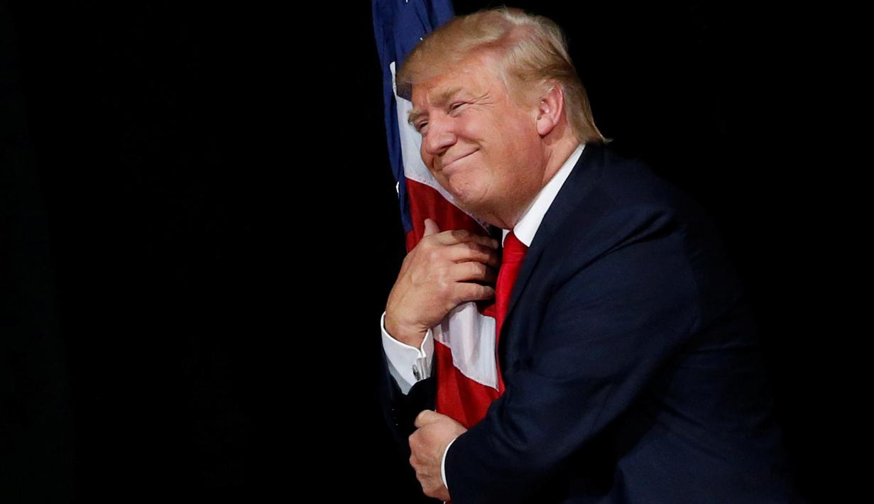 Ekspresi Donald Trump saat memeluk bendera AS pada kampanye di Tampa, Florida, AS (24/10). Pemilihan umum Presiden AS 2016 akan diadakan pada hari Selasa, 8 November 2016 dan menjadi pilpres empat tahunan ke-58. (REUTERS/Jonathan Ernst)