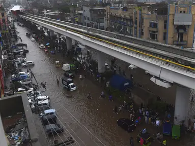Sejumlah warga beraktivitas di bawah jembatan komuter line yang banjir setelah hujan lebat di Lahore (16/7/2019). Di Kashmir yang dikelola Pakistan, para pejabat pemerintah mengatakan sedikitnya 23 orang tewas setelah hujan lebat memicu banjir bandang. (AFP Photo/Arif Ali)