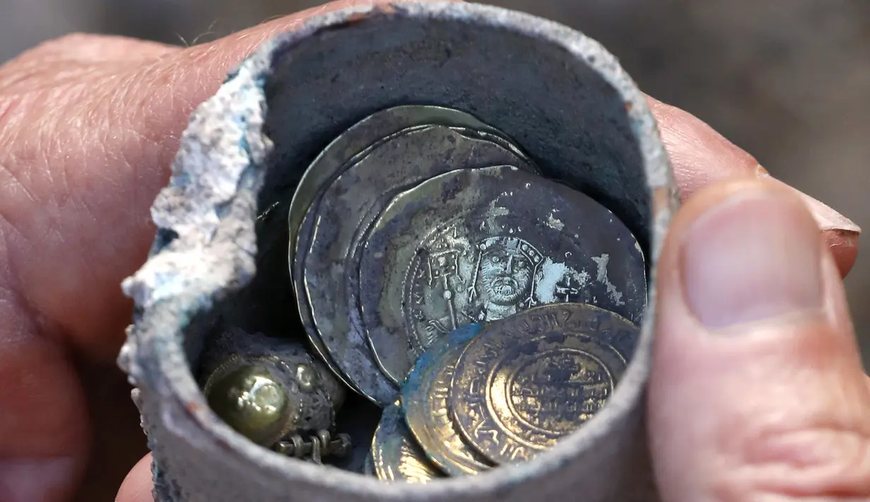 Sebuah bejana perunggu berisi koin emas kuno dan anting-anting ditemukan di sebuah situs penggalian di kota Mediterania Kaisarea, Israel, Senin (3/12). Koin-koin emas dalam bejana tersebut diperkirakan dibuat pada akhir abad ke-11. (JACK GUEZ/AFP)