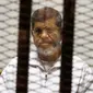 Mantan Presiden Mesir Mohammed Morsi duduk dalam penjara terdakwa di saat menjalani sidang di Akademi Kepolisian Nasional, Kairo, Mesir, 8 Mei 2019. Mohammed Morsi meninggal dalam sidang pengadilan pada Senin 17 Juni 2019 waktu setempat. (AP Photo/Tarek el-Gabbas, File)