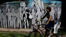 Pesepeda melewati sekolah dasar "Escuela General Las Heras" milik Lionel Messi di Rosario, Argentina, 18 April 2018.  Mural yang menampilkan Messi dilukis oleh siswa dan guru sekolah dengan bantuan seniman lokal Ruben Perez Barrios. (AP/Natacha Pisarenko)