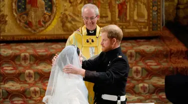 Pangeran Harry membuka tabir Meghan Markle yang disaksikan Uskup Agung Canterbury Justin Welby saat pernikahan mereka di Kapel St. George, Kastil Windsor, Inggris, Sabtu (19/5). Keduanya resmi menjadi suami istri. (Owen Humphreys/pool photo via AP)