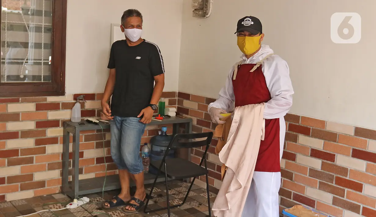 Tukang cukur mengenakan APD usai memotong rambut di halaman rumah pelanggan, Kelapa Dua, Depok, Jawa Barat, Senin (27/4/2020). Penerapan PSBB Kota Depok membuat tukang cukur tersebut menerima jasa panggilan ke rumah dan mengenakan APD untuk mencegah penularan COVID-19. (Liputan6.com/Herman Zakharia)