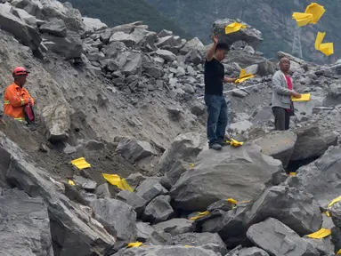 Keluarga korban melemparkan kertas ritual untuk menenangkan arwah orang yang tewas di lokasi tanah longsor di desa Xinmo, Sichuan, China (25/6). Sekitar 118 orang hilang diduga tertimbun bebatuan akibat longsor ditempat tersebut. (AP Photo / Ng Han Guan)