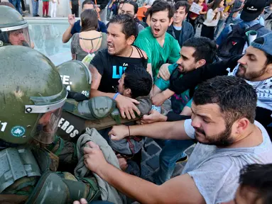 Para pengunjuk rasa mencoba membebaskan rekannya yang ditahan oleh polisi anti huru hara saat demonstrasi di luar kedutaan AS di Santiago, Chili (14/4). Mereka melakukan aksi menentang serangan AS ke Suriah. (AP / Esteban Felix)
