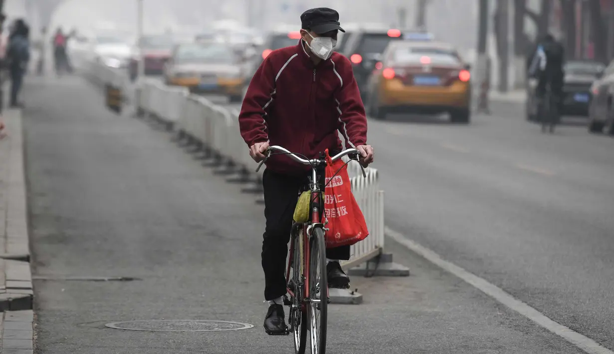 Seorang pria mengenakan masker mengendarai sepedanya di jalan pada hari yang tercemar polusi udara di Beijing, China (2/4). (AFP Photo/Fred Dufour)