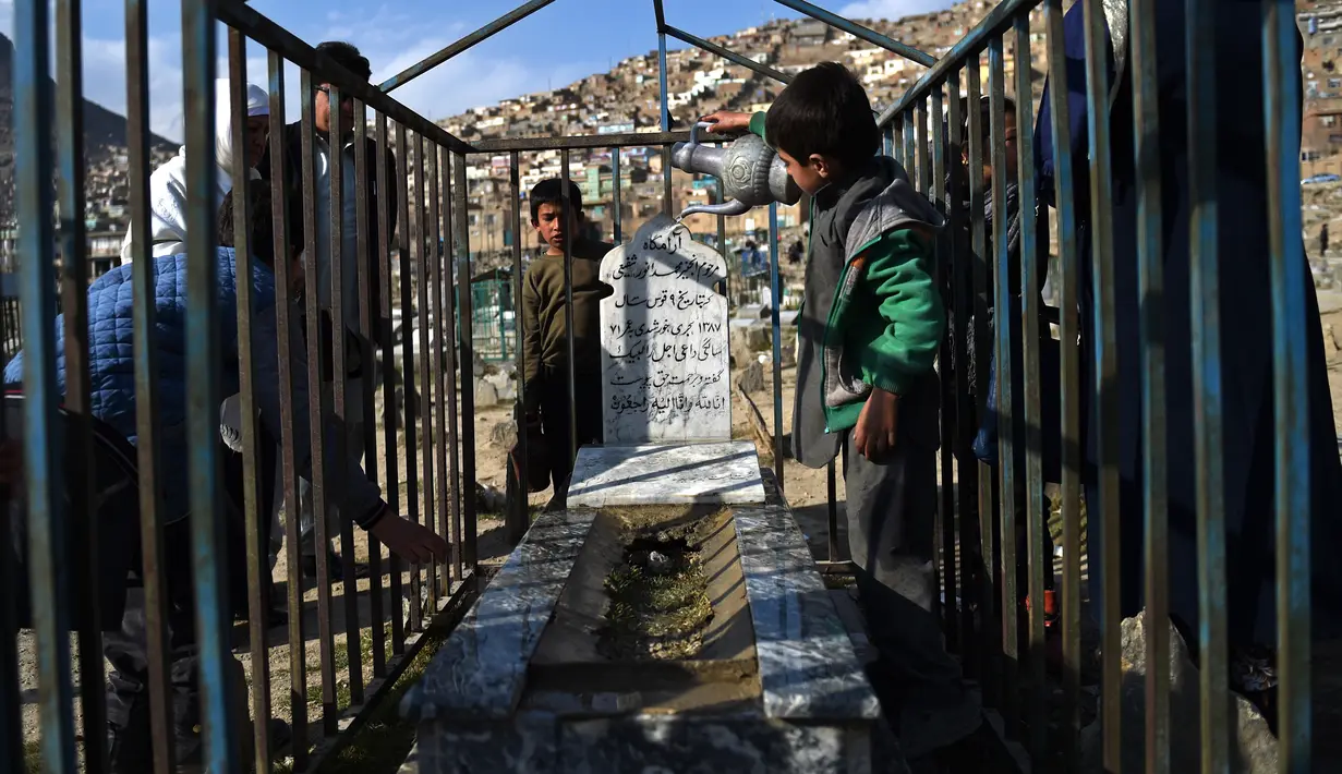 Bocah penjual air, Afghan Zilgai (9), menyiram salah satu makam kerabat dari seorang peziarah di pemakaman Kart-e-Sakhi, Kabul, 20 Februari 2016. Afghan setiap hari menjual air kepada para peziarah dengan penghasilan 1,5 USD/hari. (AFP PHOTO/Wakil KOHSAR)