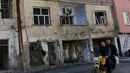  Warga melewati bangunan yang rusak akibat konflik antara Militer Turki dan Militan Kurdi di Turki, (7/12). Militan Kurdi dan afiliasinya Partai Pekerja Kurdi (PKK) dilabeli oleh pemerintah Ankara sebagai kelompok teroris. (REUTERS/Murad Sezer)