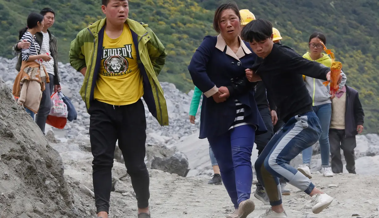 Keluarga dan kerabat korban menuju lokasi sambil membawa alat ritual untuk menenangkan arwah orang yang tewas di lokasi tanah longsor di desa Xinmo, Sichuan, China (25/6). (AP Photo / Ng Han Guan)