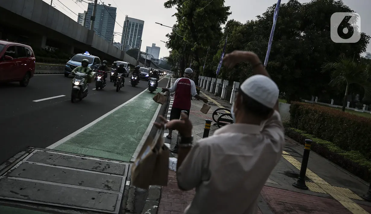 Petugas mengajak pengendara untuk mengambil takjil di Kompleks Masjid Al-Azhar, Jakarta, Kamis (15/4/2021). Pengelola masjid menyiapkan 500 bungkus takjil setiap harinya untuk pengendara yang dibagikan dengan sistem drive thru untuk mencegah penyebaran COVID-19. (Liputan6.com/Johan Tallo)