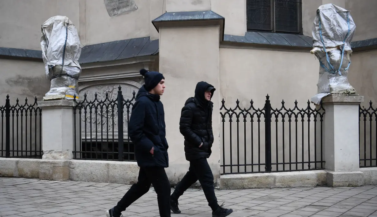 Pejalan kaki berjalan melewati patung-patung yang dibungkus dengan plastik di Katedral Latin di Lviv, 5 Maret 2022. Warga kota Lviv membungkus semua patung yang ada di kota tersebut untuk melindungi warisan sejarahnya dari kerusakan akibat serangan di tengah konflik Rusia-Ukraina. (Daniel LEAL/AFP)
