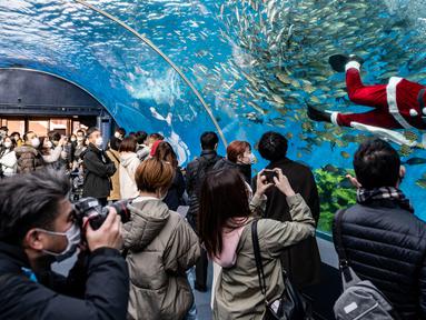 Seorang penyelam berpakaian seperti Sinterklas (kanan) memberi makan ikan dalam akuarium disaksikan pengunjung dan fotografer di Yokohama Hakkeijima Sea Paradise, Yokohama, Jepang, 10 Desember 2021. Walau populasi umat Kristiani hanya 1 persen, perayaan Natal di Jepang tetap meriah.(Philip FONG/AFP)