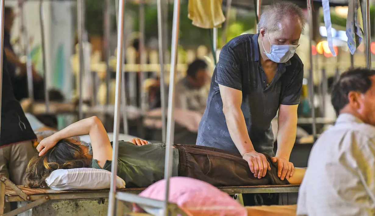 Tukang pijat sedang melayani pelanggan di sebuah stan terbuka di Nanning, di wilayah selatan Guangxi, China (21/6/2020). Par tukang pijat membuka layanannya hanya bermodalkan tempat tidur besi yang dilapisi alas tikar dan bantal lengkap dengan atap berpenutup terpal. (China OUT/STR/AFP)