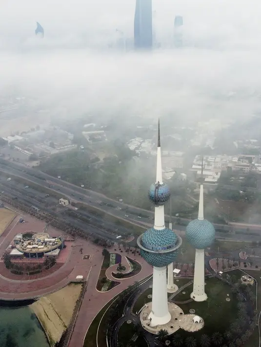 Kabut pagi terlihat menutupi Kuwait Towers dalam foto udara yang ditunjukkan pada Selasa (14/3/2023). Terlihat gedung-gedung pencakar langit menembus awan yang seakan-akan seperti kota langit. (Photo by Yasser Al-Zayyat / AFP)