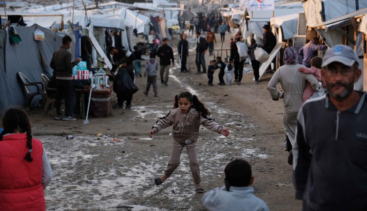 Warga masih menghadapi krisis kemanusiaan, termasuk kekurangan makanan, air, dan layanan kesehatan. Tampak dalam foto, anak-anak berjalan dan bermain di sepanjang jalan berlumpur di dalam kamp pengungsian di Jabalia, di bagian utara Jalur Gaza, Minggu 7 Desember 2025. (AP Photo/Jehad Alshrafi)
