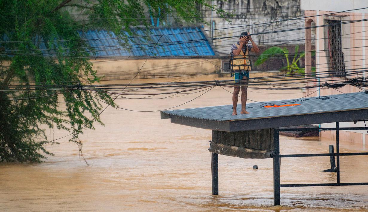 Diketahui, Thailand secara rutin mencatat bahwa hujan lebat biasanya terjadi sejak Juni hingga September. Tampak dalam foto, seorang pria bereaksi saat berdiri di atas atap di samping banjir bandang yang tinggi di Hat Yai, Provinsi Songkhla, Thailand selatan, pada 26 November 2025. (Arnun Chonmahatrakool/THAI NEWS PIX/AFP)