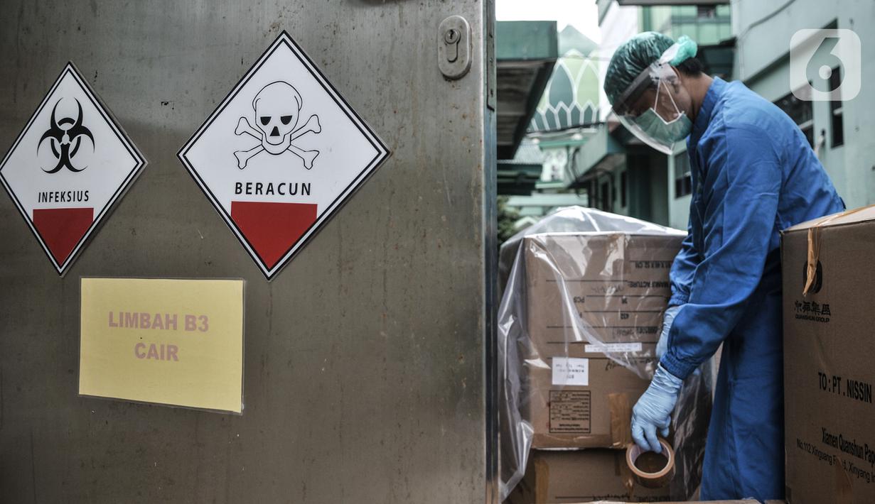 Petugas berpakaian APD mengemas limbah Covid-19 ke dalam kardus berlapis plastik di Tempat Penyimpanan Sementara Limbah B3 di Labkesda DKI Jakarta, Selasa (4/8/2020). Setiap kantong berisi limbah Covid-19 dibawa ke ruang sterilisasi sebelum diangkut ke tempat pembuangan. (merdeka.com/Iqbal Nugroho)