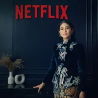 Dian Sastrowardoyo tampil mengenakan kebaya velvet warna navy dengan detail bordiran pita, dipadu kain batik sebagai bawahan dari Saptodjojokartiko. [@netflixid]